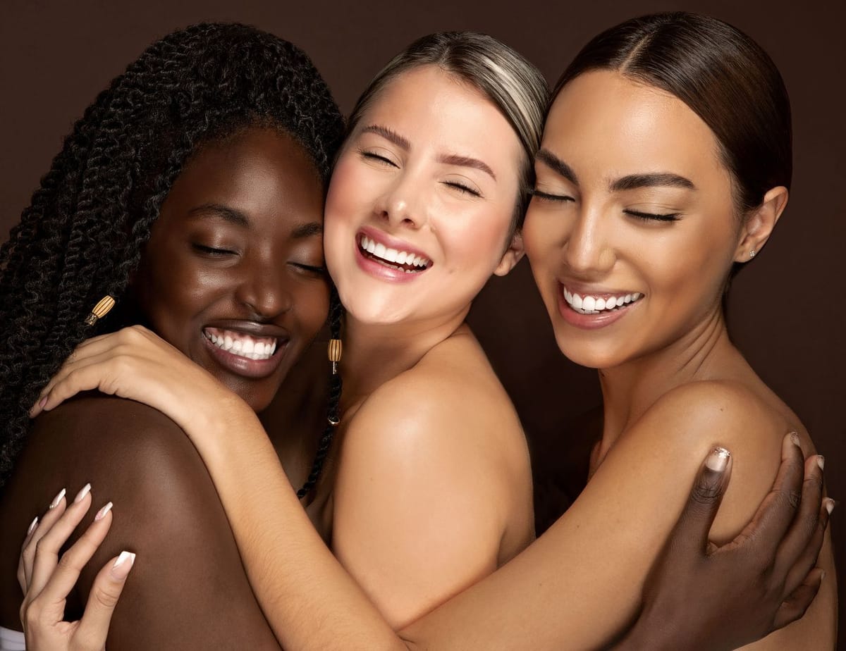 Tres modelos con piel luminosa abrazadas y sonriendo